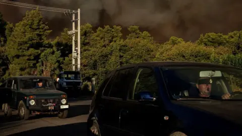 Reuters - La gente conduce mientras se eleva el humo de un incendio forestal en el pueblo de Varnavas, cerca de Atenas, Grecia, el 11 de agosto de 2024.