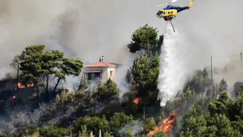 Reuters - Un helicóptero sobrevuela y arroja agua sobre un incendio cerca de una casa.