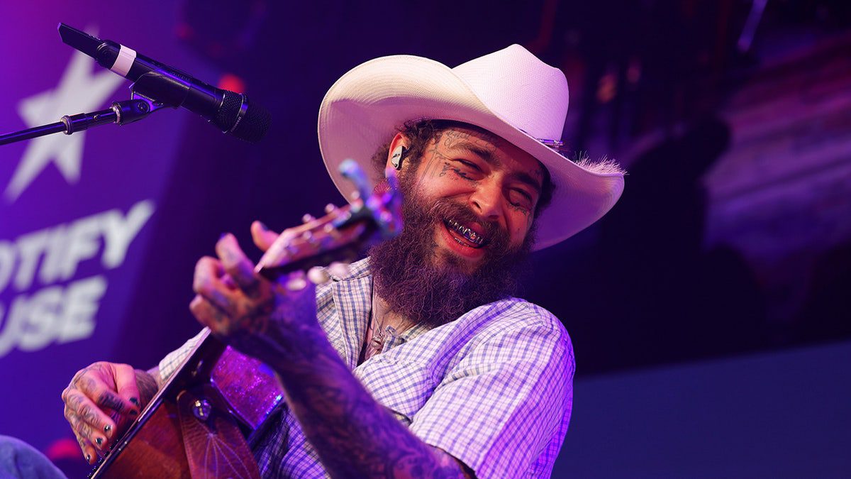 El músico Post Malone usa un sombrero de vaquero mientras toca la guitarra.