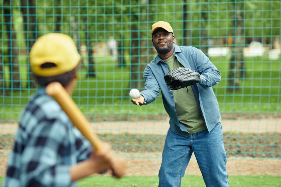 Un hombre africano atrapa una pelota con un guante que le lanza su hijo durante un partido de béisbol al aire libre.